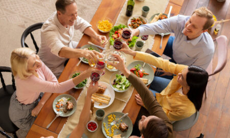 Люди сидят за праздничным столом, едят, пьют и произносят тосты