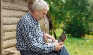 Пожилой житель села сидит за ноутбуком.