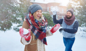 Мужчина бросает снежок в смеющуюся женщину