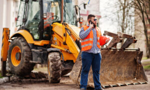 Рабочий стоит у экскаватора