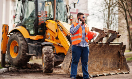 Рабочий стоит у экскаватора