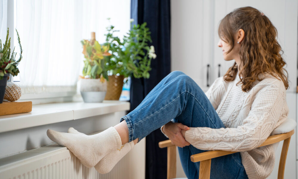 Девушка греет ноги у батареи