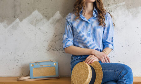 Девушка сидит у стены и держит соломенную шляпу.