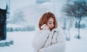 Девушка в тёплой куртке стоит на заснеженной улице