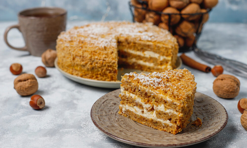 Торт медовик на тарелке, кружка на фоне