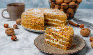 Торт медовик на тарелке, кружка на фоне