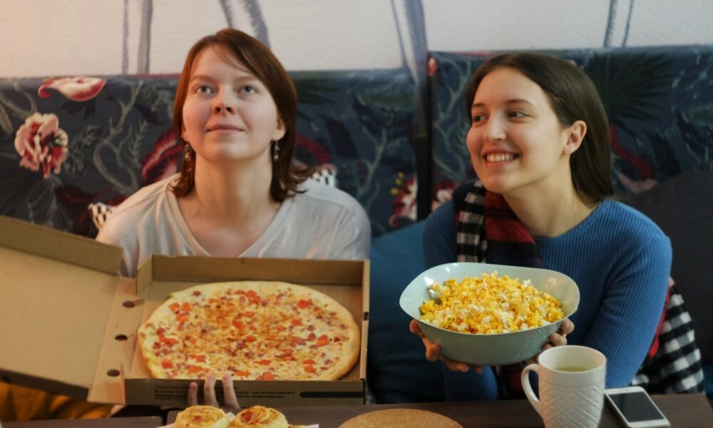 Две девушки смотрят кино и держат в руках пиццу и попкорн