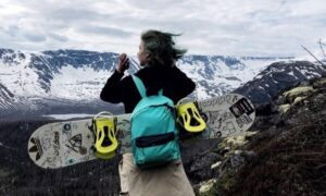 Девушка со сноубордом на фоне заснеженных гор.