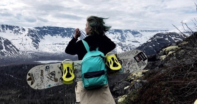 Девушка со сноубордом на фоне заснеженных гор.