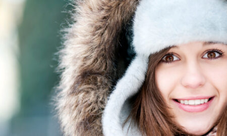 девушка улыбается в шапке-ушанке и капюшоне с мехом