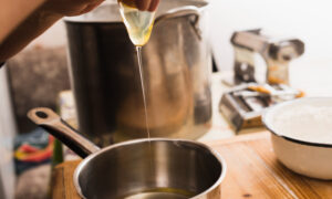 выливает куриное яйцо в сотейник