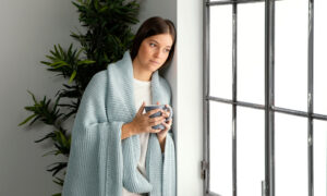 Женщина греется в пледе зимой у окна