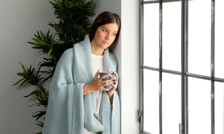 Женщина греется в пледе зимой у окна