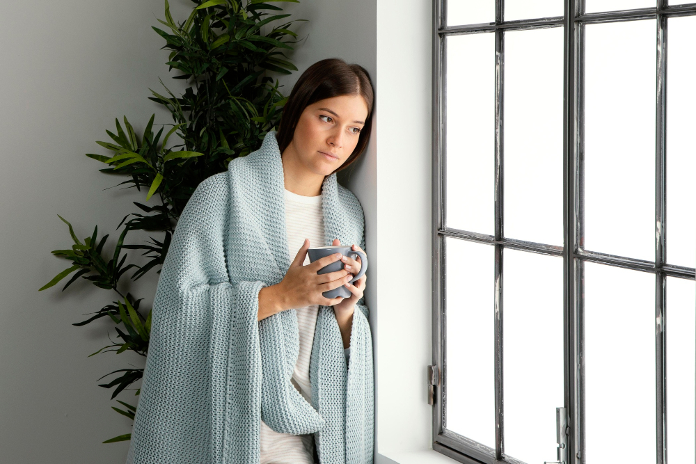 Женщина греется в пледе зимой у окна