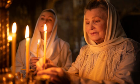 Пожилая женщина зажигает свечи в церкви