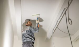 рабочий красит потолок