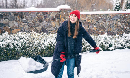 Женщина убирает снег у частного дома