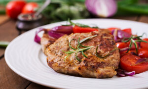 Сочный свиной стейк с розмарином и помидорами на белой тарелке