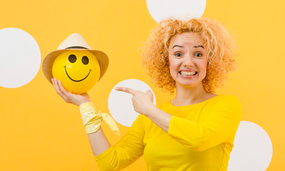 Девушка в желтом показывает на смайлик, который держит в руках