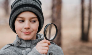 Ребенок в вязаной шапке смотрит в лупу