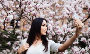 Девушка делает селфи на фоне цветущих весной веток.