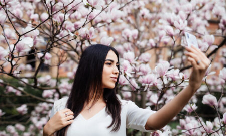 Девушка делает селфи на фоне цветущих весной веток.