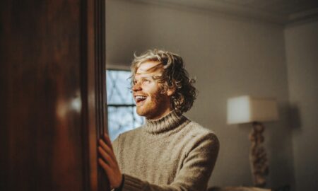 Мужчина в свитере стоит в комнате и улыбается
