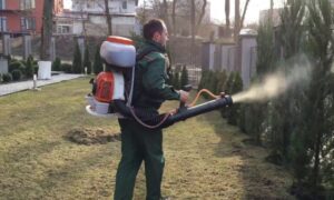 мужчина опрыскивает сад из ранцевого бака