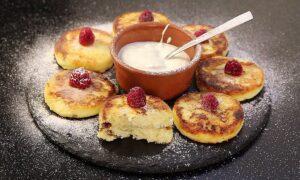 сырники, посыпанные сахарной пудрой, со сметаной и малиной