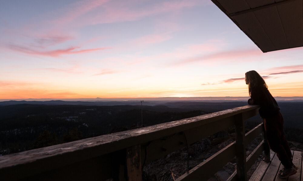 Девушка смотрит в вечернее небо с балкона.
