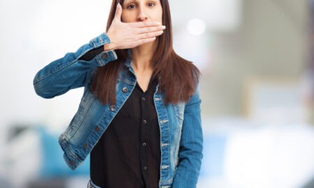 Девушка в джинсовой куртке закрывает рот ладонью.
