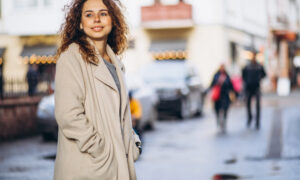 Девушка в плаще гуляет по оживленной улице.