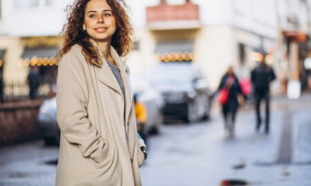 Девушка в плаще гуляет по оживленной улице.