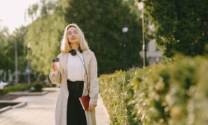 Девушка со стаканчиком кофе идет по аллее.