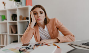 Девушка за столом в офисе задумчиво смотрит перед собой.