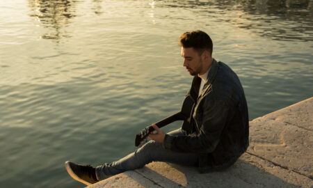 Парень сидит у воды с гитарой.