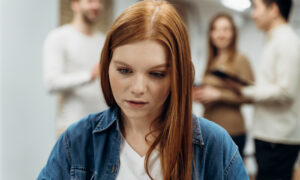 Девушка пытается работать с ноутбуком, пока ее коллеги за спиной беседуют.