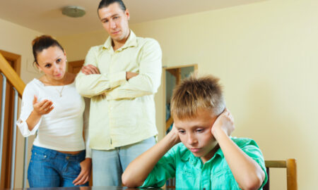Родители отчитывают сына, сидящего за столом, за провинность.