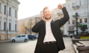 Парень идет по улице, разговаривает по телефону и радуется своей удаче.