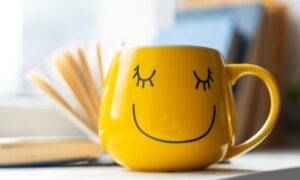 Желтая кружка с улыбающимся смайлом на столе.