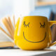 Желтая кружка с улыбающимся смайлом на столе.