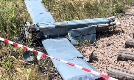 Обломки сбитого беспилотника самолетного типа на земле, огражденные сигнальной лентой.