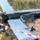 Обломки сбитого беспилотника самолетного типа на земле, огражденные сигнальной лентой.
