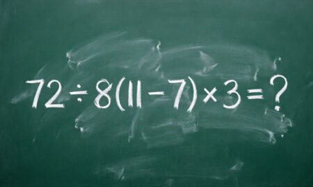 Снимок школьной зеленой доски крупным планом, на которой белым мелом по центру написано математическое выражение 72 ÷ 8(11 − 7) × 3 = ?.